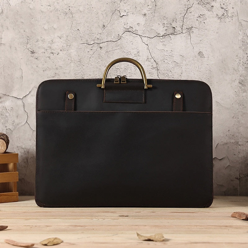 Black Crazy Horse leather men's business handbag with brass handle on wooden surface against textured wall background