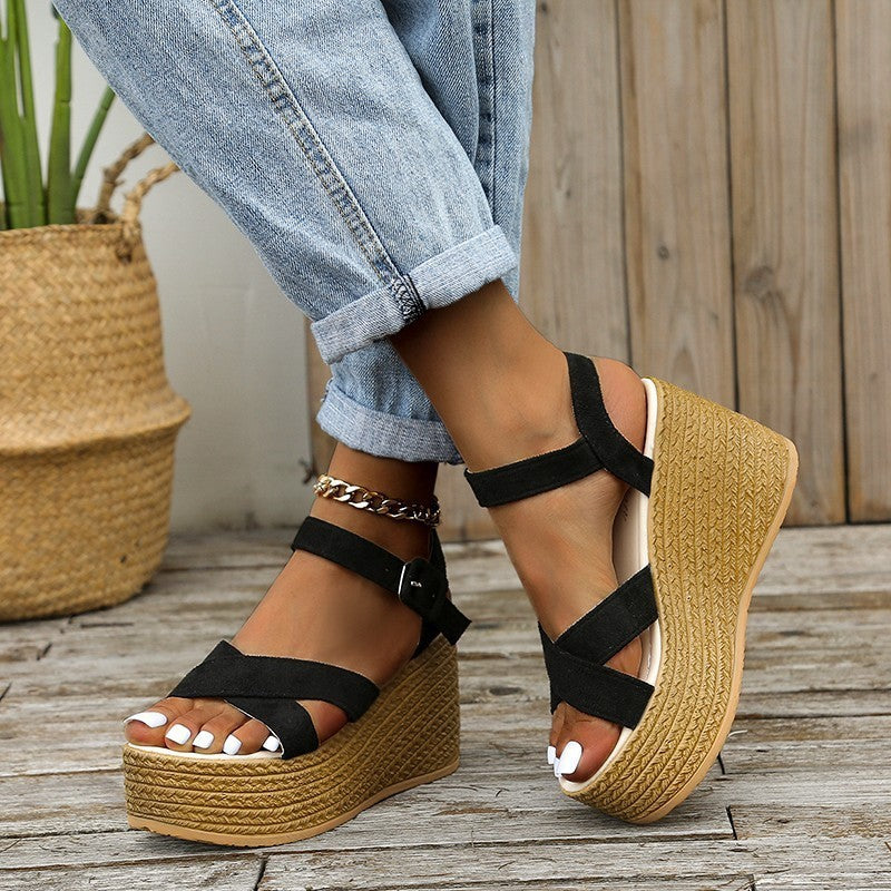 Women's black suede platform sandals with buckle straps and woven wedge heels worn with rolled-up jeans
